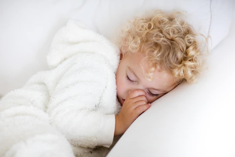 Young blond boy sleeping on couch sucking his thumb.