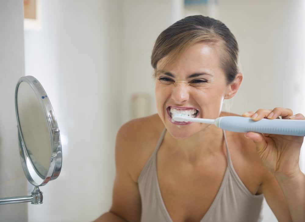 Young woman with grimace brushing teeth.