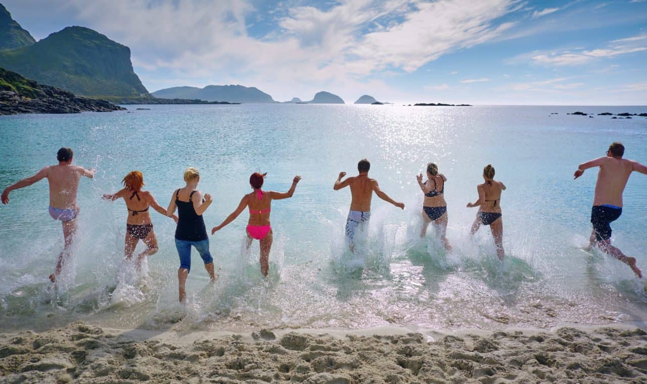 Men and women in bathing suits jumping and splashing in cold water having fun.