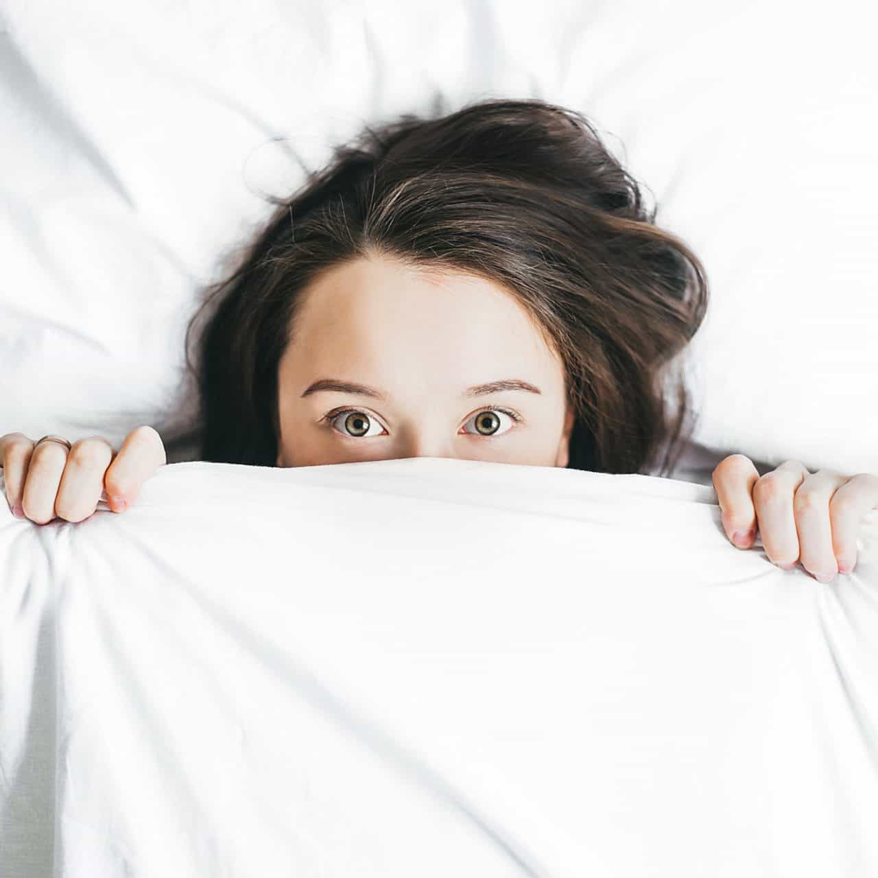 Woman awake in bed with blanket over her mouth and nose