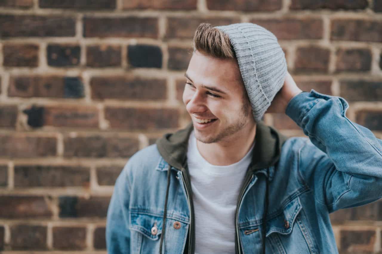 Young man wearing knit cap and denim jacket with big smile