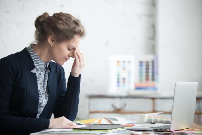 The Reason Your Head Hurts Might Be Your Teeth Woman at work with headache