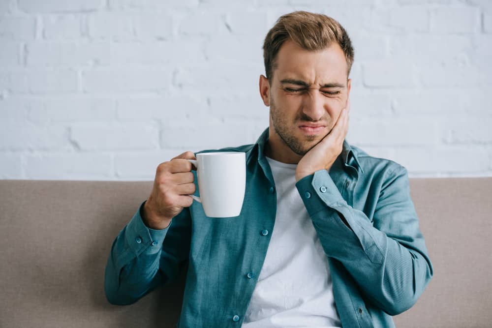 Man holding face with tooth pain drinking hot beverage