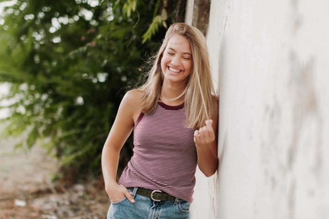 young woman leaning on wall near trees