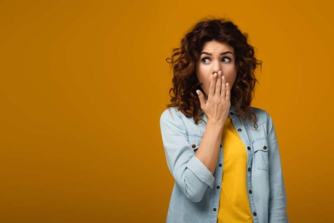 redheaded woman with hand over mouth and bad breath