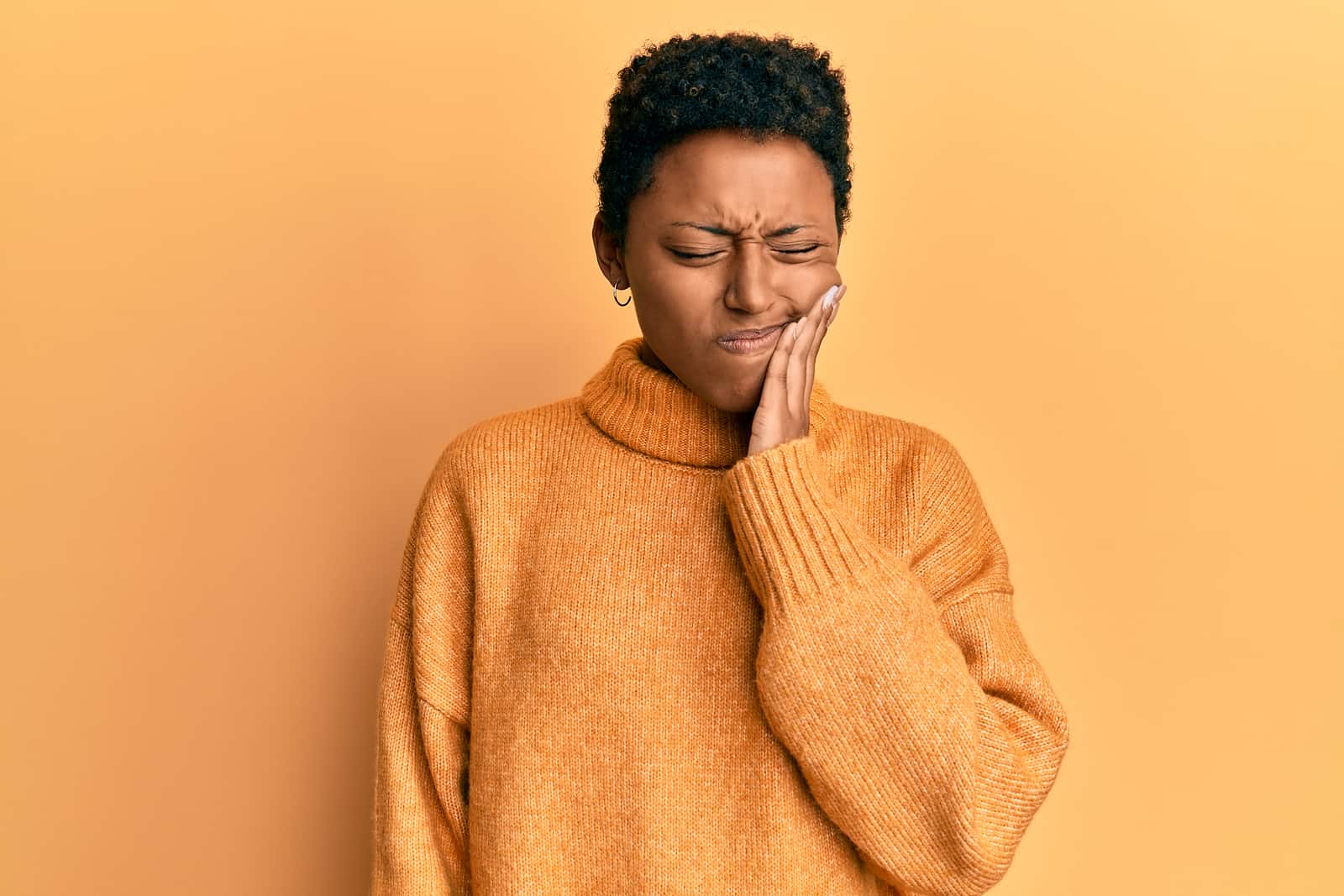 African American woman with toothache against orange background.