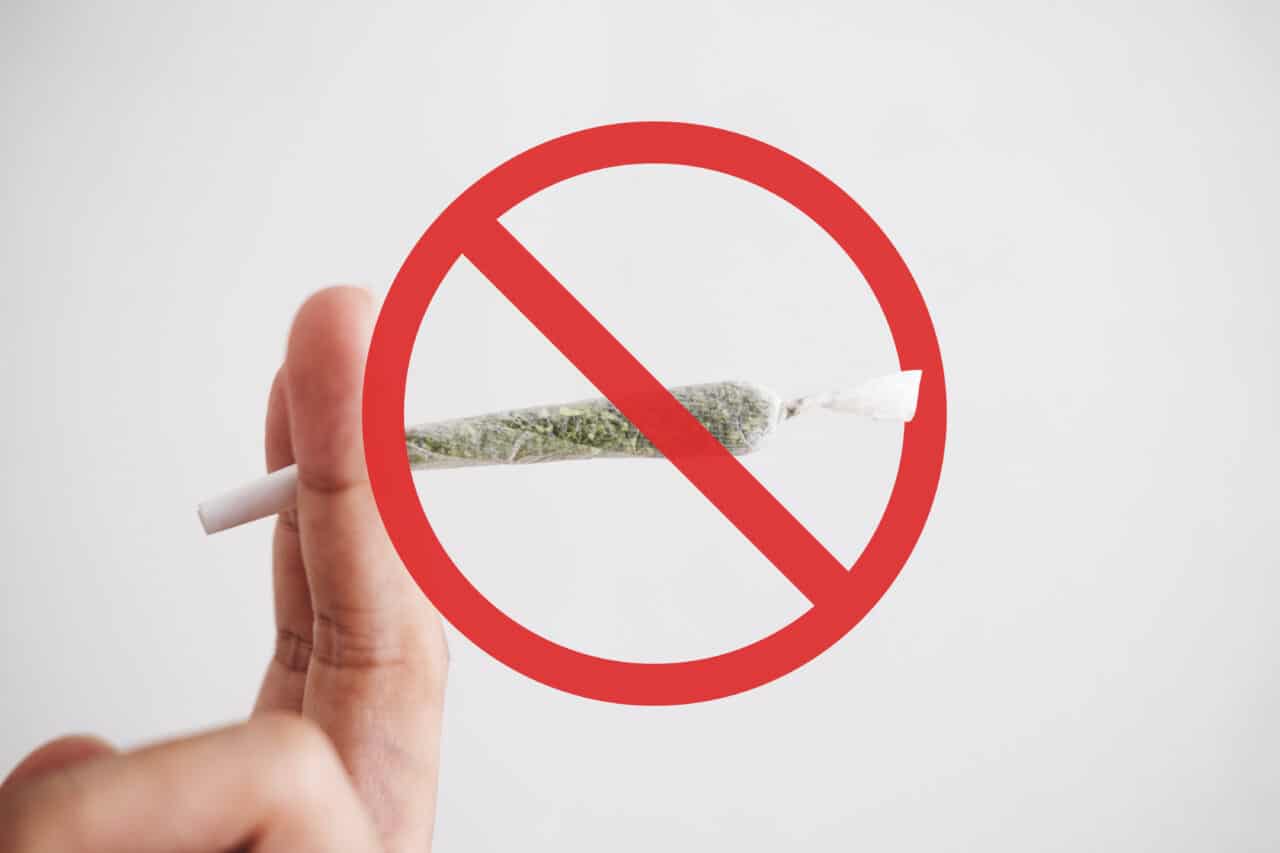 A joint sits in between two fingers with a red stop sign over it, encouraging people to not use marijuana before receiving anesthesia for a dental appointment. 