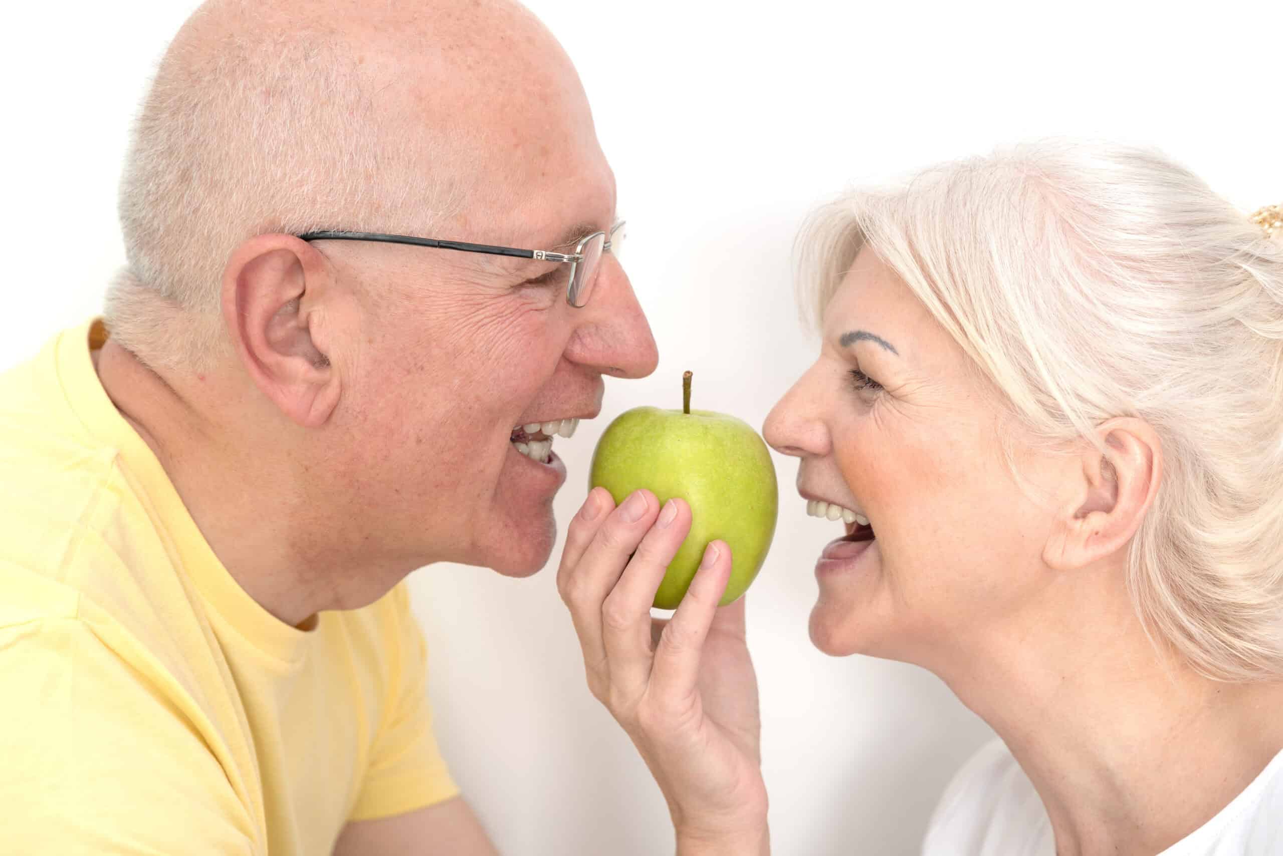 Senior couple with green apple. Healthy teeth, strong dental implants, healthy nutrition concept