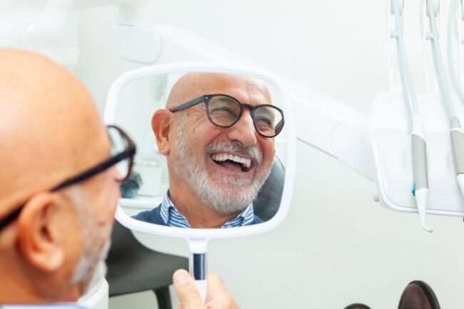 Happy senior dental patient smiling in a mirror.